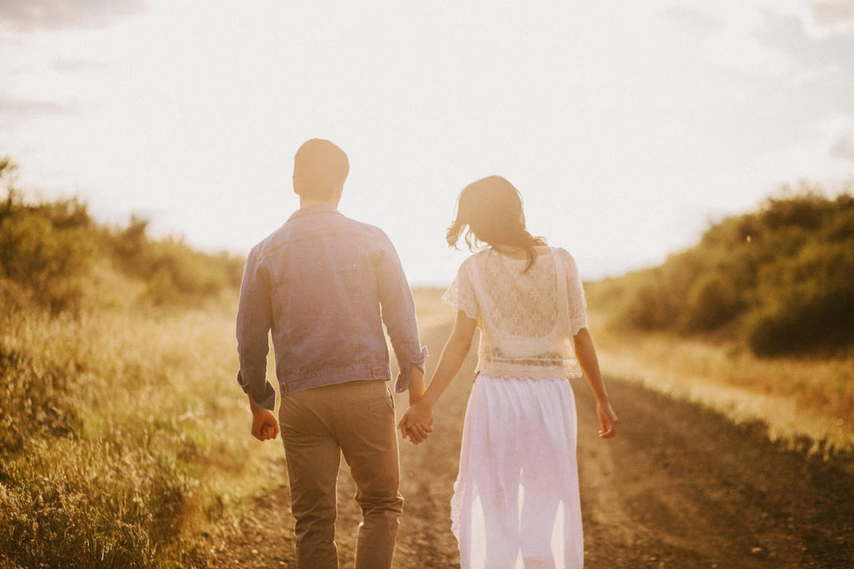 Casal de mãos dadas caminhando em uma estrada de campo ao pôr do sol
